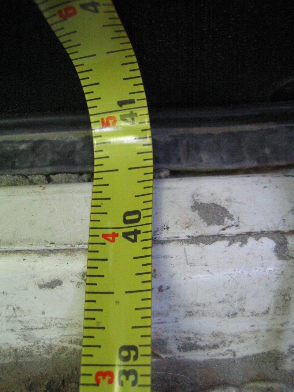 Yellow measuring tape with inch and foot markings, curved, measuring an unseen surface