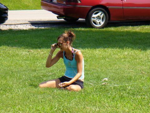 1991 Ford Probe - A woman sits on the grass, adjusting her sunglasses, with the rear of a red car visible behind her.
