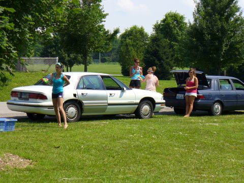 1991 Ford Probe - Two sedans are parked on a grassy area with trees in the background and people standing nearby.