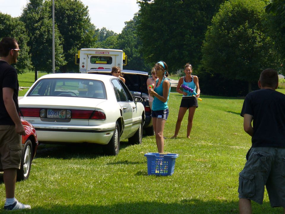 White sedan parked on grass, people with water guns around it