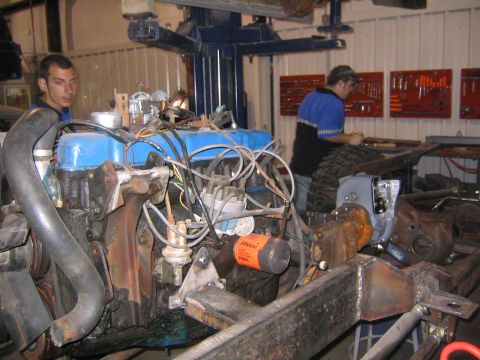 1982 Ford Bronco - Workshop scene with engine and chassis assembly, two mechanics working.