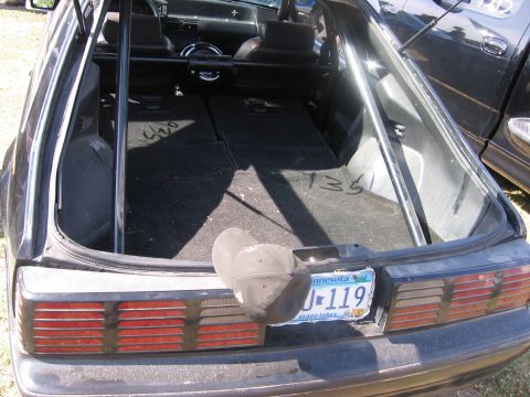 1989 Ford Mustang - The rear of a black hatchback with a roll cage and folded seats is visible, with a Minnesota license plate attached.