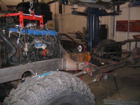 1982 Ford Bronco - Workshop scene with an engine and chassis assembly. A large off-road tire is visible.
