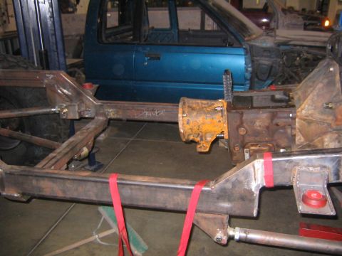 1982 Ford Bronco - The frame and drivetrain components of a vehicle are shown, with a blue truck cab in the background.