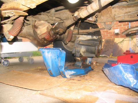 1978 Ford Bronco - Underneath view of a vehicle's drivetrain during transmission removal, with tools and fluids present.