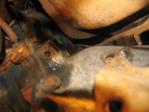 1978 Ford Bronco - Close-up view of a heavily rusted engine transmission mount, showing bolts and part of an exhaust pipe.