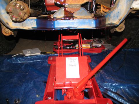 1978 Ford Bronco - Transmission fluid is draining from the vehicle's undercarriage onto a red jack and blue tarp.