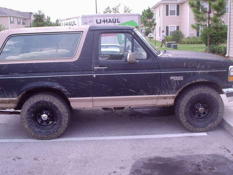 Muddy black and tan Ford Bronco side view with black steel wheels, parked near a U-Haul truck