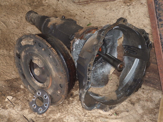 Disassembled automatic transmission with flywheel and bell housing separated. Shaft is visible