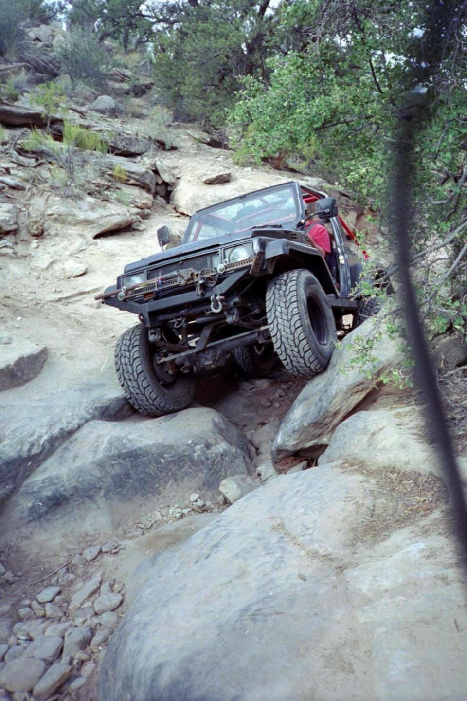 Black open-top compact 4x4 crawling over boulders, front 3/4, winch bumper