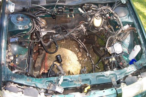 1995 Ford Taurus - The engine bay of a green 1995 Ford Taurus is shown with the engine removed, revealing the complex wiring and internal components.
