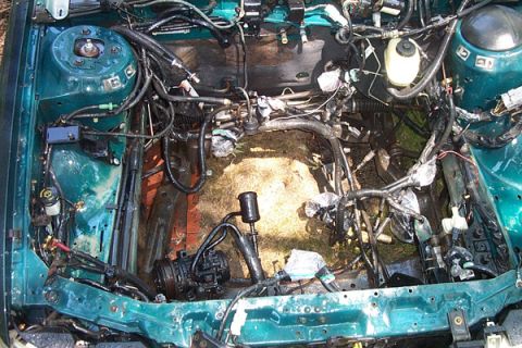 1995 Ford Taurus - The engine bay of a green vehicle, with most components and wiring removed, revealing the empty space where the engine once was.