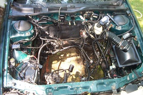 1995 Ford Taurus - Engine bay of a green car, engine has been removed, revealing internal components and wiring.