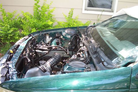 1995 Ford Taurus - The engine bay of a green vehicle is shown with various components and wiring. The vehicle's year is not identifiable from the image.