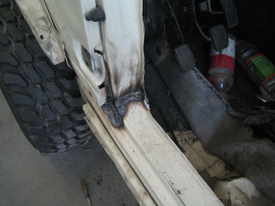 White vehicle door frame with fresh welds, next to a large off-road tire
