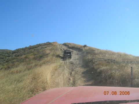 1985 Ford Bronco - Off-road vehicle ascends a dusty hill under a clear blue sky. Taken from another vehicle.