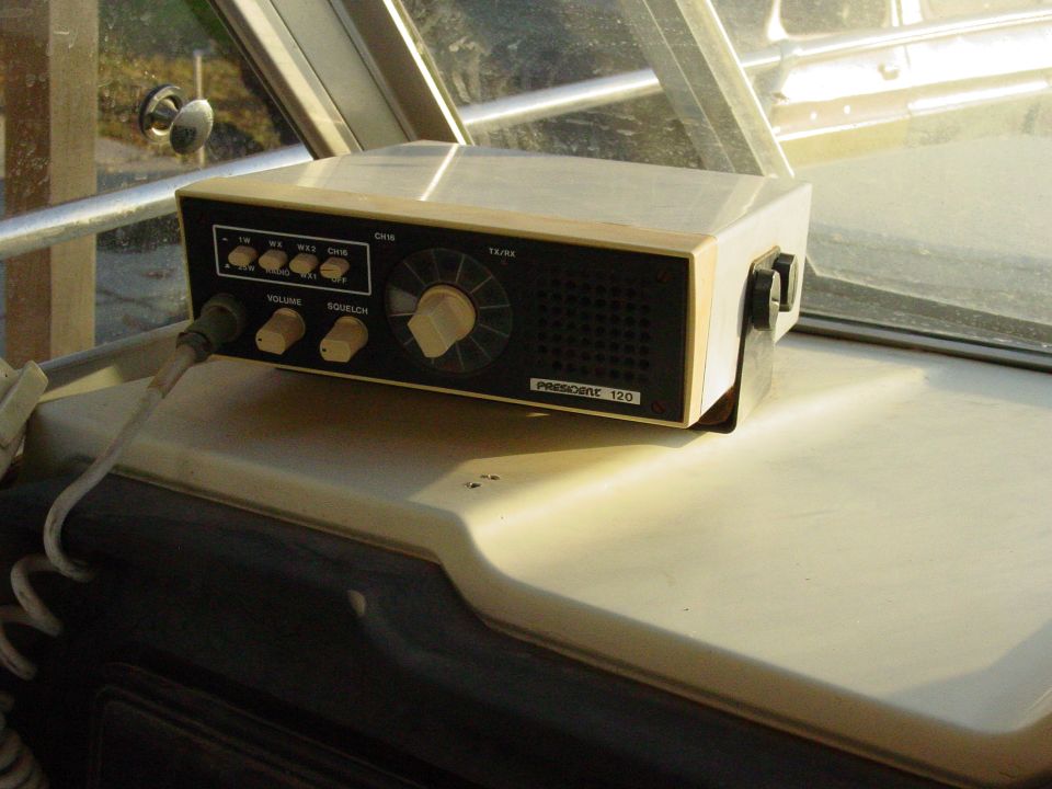Cream and black President 120 marine radio on boat dashboard by a window.