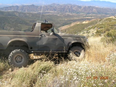 1985 Ford Bronco - A lifted Ford Bronco sits on a hillside overlooking a valley, with mountains in the distance.