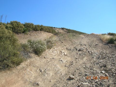 1985 Ford Bronco - A off-road trail winds uphill through dry brush and rocks on a clear day.