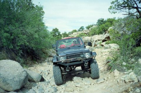 1982 Ford Customline - A Suzuki Samurai navigates a rough, rocky terrain on a sunny day.