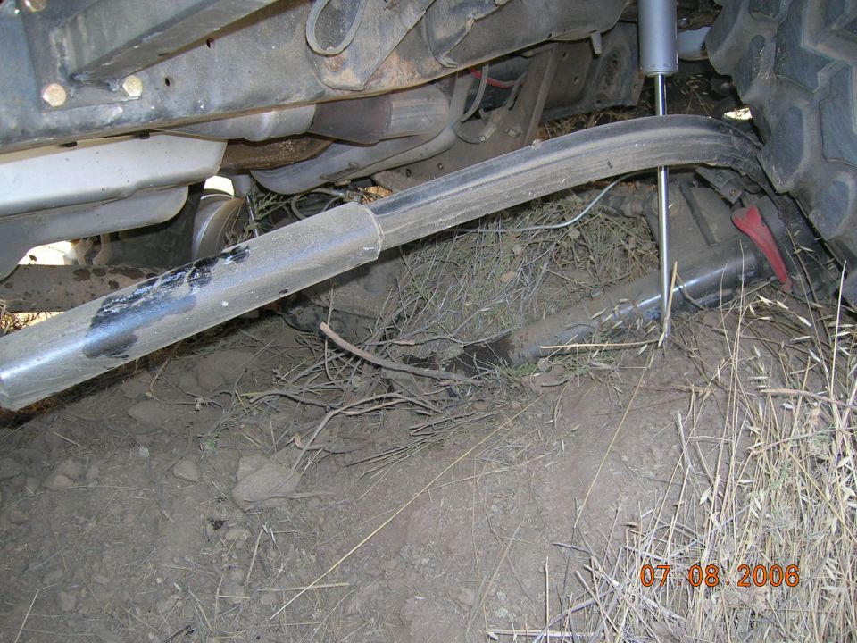 Undercarriage view of a vehicle showing a bent control arm and exhaust pipe, with a shock absorber visible