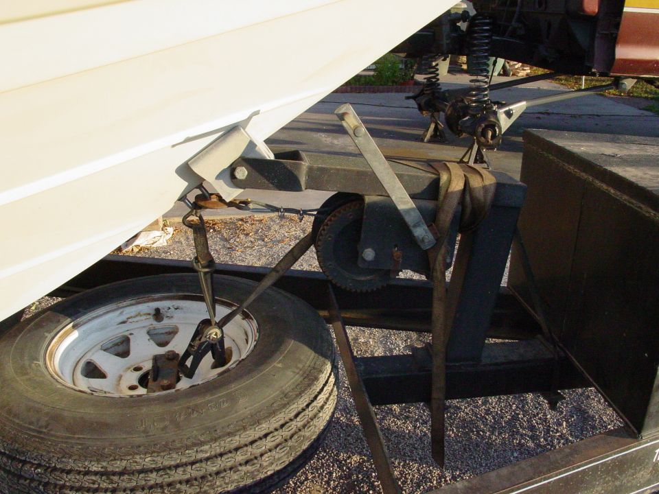 Boat trailer winch, jack and spare tire secured with strap and chain on gravel