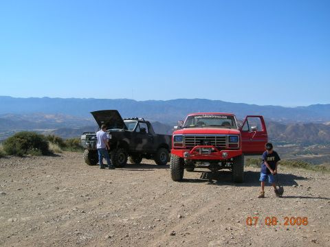 1985 Ford Bronco - Two Ford trucks parked on a dirt road with a scenic mountain view.