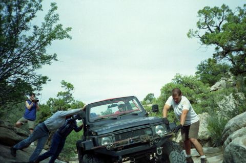 1982 Ford Customline - People push a black off-road vehicle on a rocky, wooded trail.