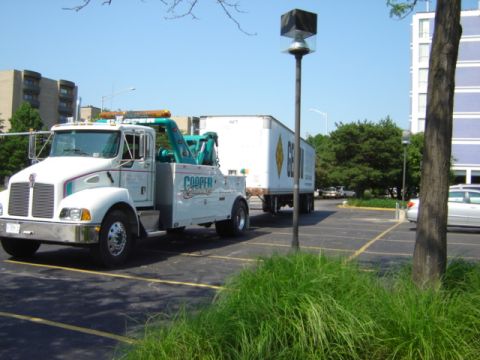 1992 Ford Bronco - A Kenworth tow truck is seen towing a semi-trailer in a parking lot.