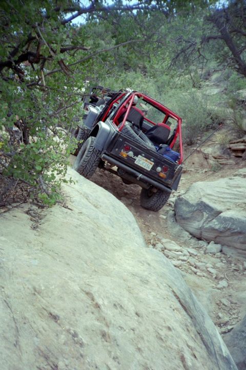 1982 Ford Customline - An off-road vehicle navigates a steep, rocky trail, its red roll cage contrasting with the dark body.