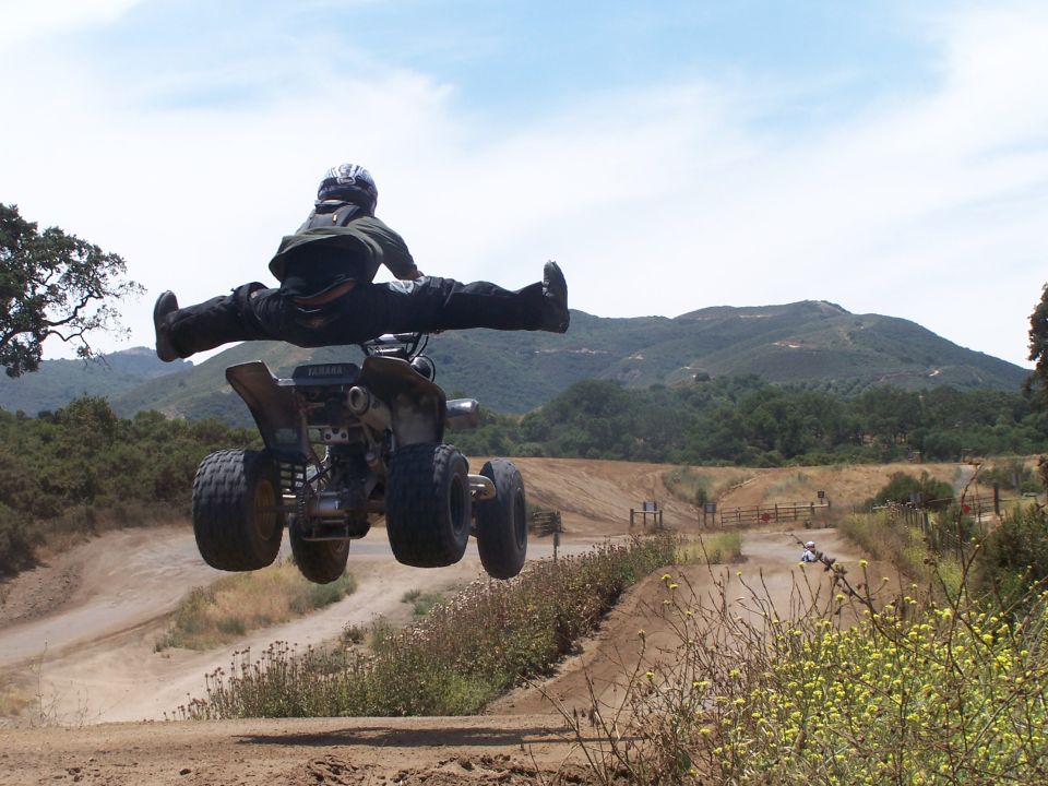 ATV rider mid-air doing a split, with mountains in background
