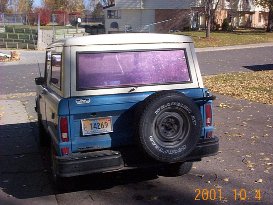 Rear view of blue Ford Bronco with tan hardtop and Goodyear spare tire mounted on tailgate, parked in driveway
