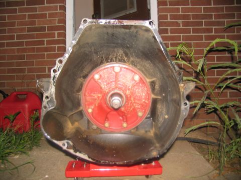1978 Ford Bronco - Transmission bell housing removed from vehicle, resting on a red dolly outside.