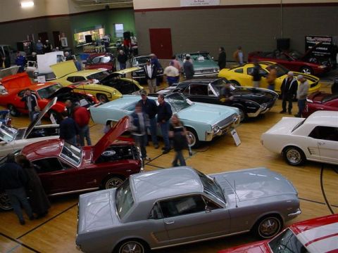 1972 Ford Ranchero - A variety of classic cars are gathered indoors for an exhibition, with attendees observing the vehicles.
