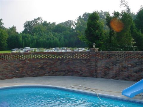 1972 Ford Ranchero - A collection of vehicles is visible behind a decorative brick wall, with a swimming pool and slide in the foreground.