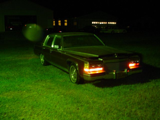 Maroon sedan with headlights and taillights on, parked on grass at night