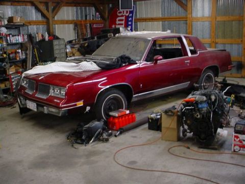 1972 Ford Ranchero - 1977 Oldsmobile Cutlass Supreme coupe in a garage with its engine removed.