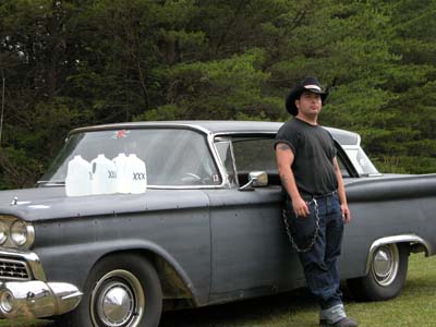 1972 Ford Ranchero - A man in a cowboy hat leans against a gray 1959 Ford Ranchero with three jugs on its hood.