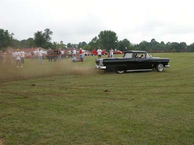 1972 Ford Ranchero - A black pickup truck with a bed drives across a grassy field, kicking up a cloud of dust.