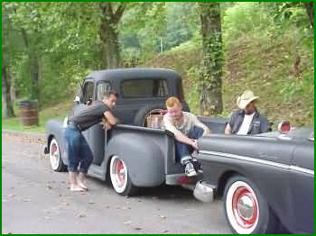 1972 Ford Ranchero - Three men are gathered in the bed of a vintage pickup truck, with a second vehicle partially visible in the foreground.