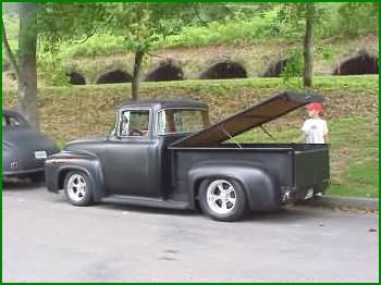 1972 Ford Ranchero - A black pickup truck with its tonneau cover raised, parked curbside with another vehicle partially visible.