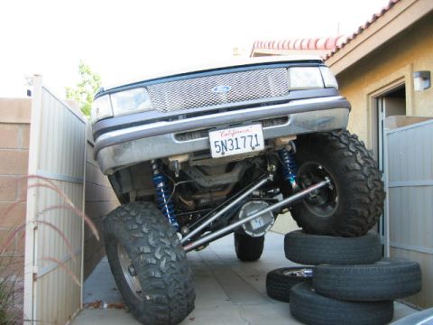 1997 Ford Ranger - Modified 1997 Ford Ranger front end is lifted on tires, parked precariously between a fence and a building.