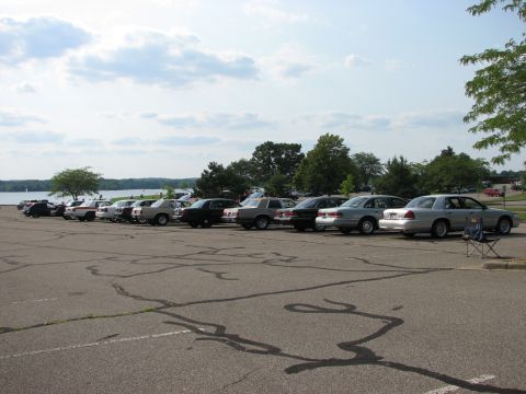 2003 Ford Crown Victoria - A row of sedans, including a 2003 Ford Crown Victoria, are parked in a lot near a body of water.