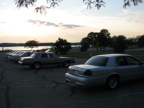 2003 Ford Crown Victoria - Several Ford Crown Victorias parked near a lake at sunset.