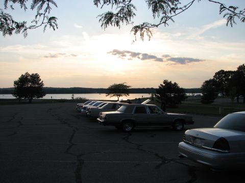 2003 Ford Crown Victoria - Cars parked by a lake at dusk, with trees and a cloudy sky overhead.