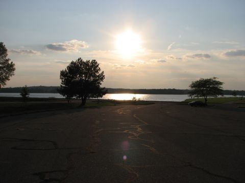 2003 Ford Crown Victoria - A lone car sits in a parking lot next to a lake as the sun sets in the sky.