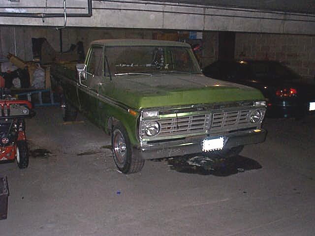 Green Ford pickup truck parked in a dim garage, front-right view