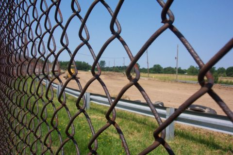 1978 Ford Bronco - A view through a rusty chain-link fence shows construction equipment and a dirt track under a clear blue sky.