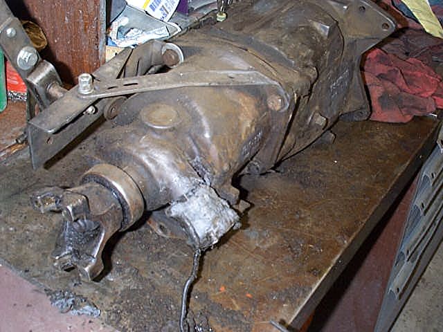 Dirty manual transmission with output yoke resting on a wooden workbench