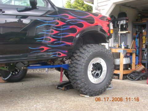 1996 Ford Bronco - A black Ford Bronco with flame decals is lifted on a jack, showing its large tires and suspension modifications.